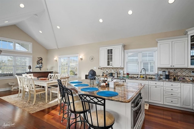 kitchen with a breakfast bar, dark wood-style flooring, stainless steel oven, a sink, and dark stone counters