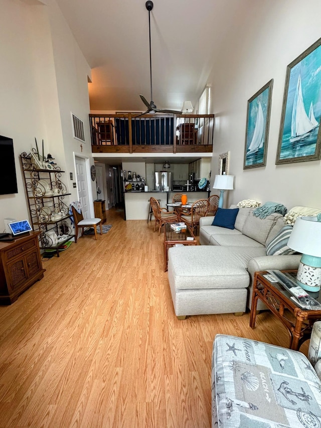 living room with a towering ceiling, ceiling fan, and light hardwood / wood-style flooring