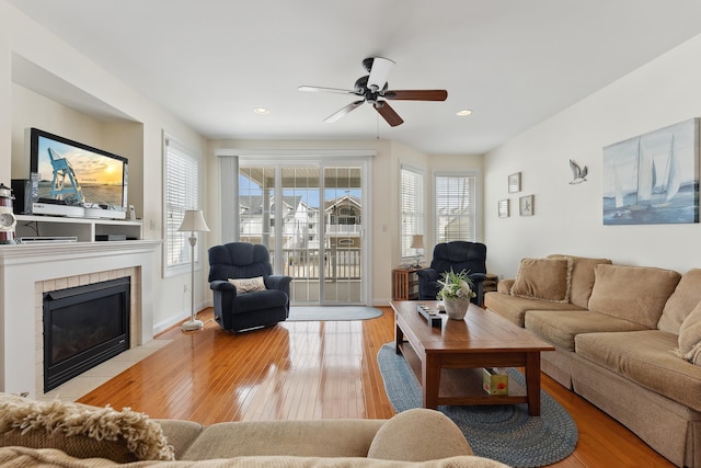 living room with a tiled fireplace, ceiling fan, and light hardwood / wood-style flooring