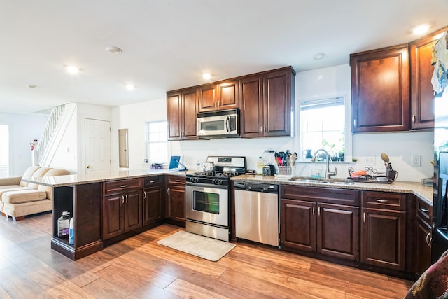 kitchen featuring open floor plan, a peninsula, stainless steel appliances, light wood-type flooring, and a sink