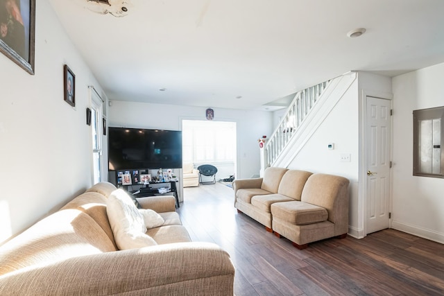 living room with dark wood-type flooring, baseboards, and stairs