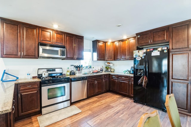 kitchen with recessed lighting, stainless steel appliances, a sink, light wood-style floors, and light stone countertops