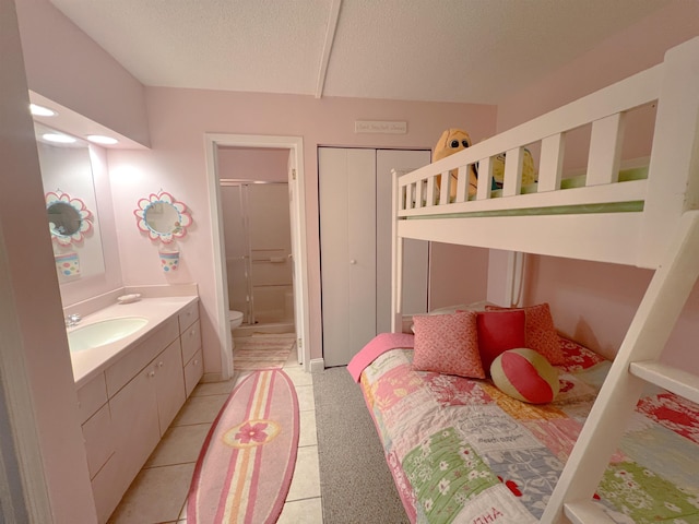 tiled bedroom featuring ensuite bathroom, sink, a textured ceiling, and a closet