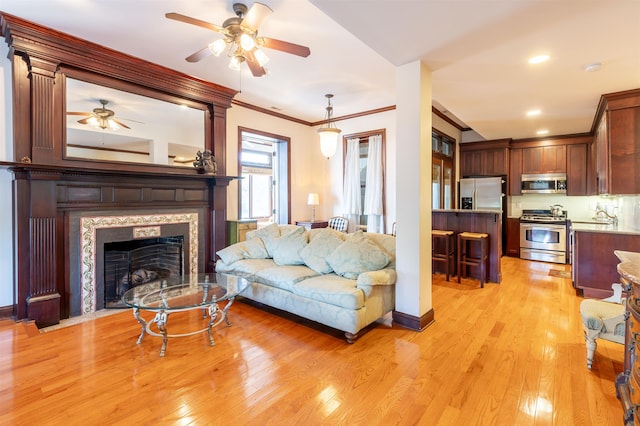 living room featuring ceiling fan, light wood-type flooring, and crown molding