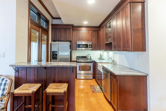 kitchen with kitchen peninsula, light wood-type flooring, stainless steel appliances, sink, and a breakfast bar area