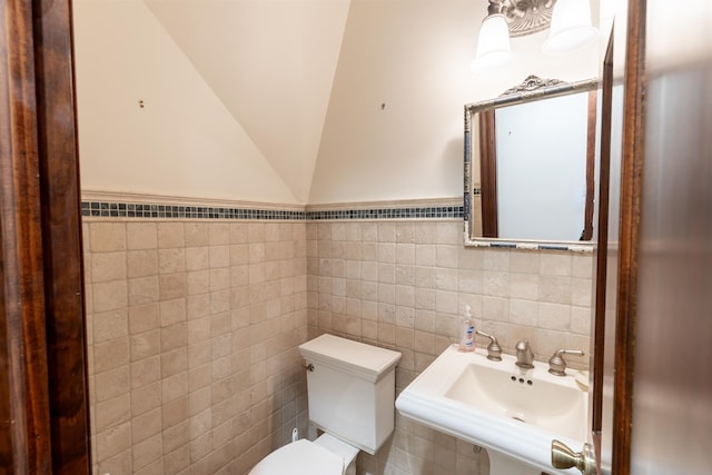 bathroom with toilet, tile walls, lofted ceiling, and sink