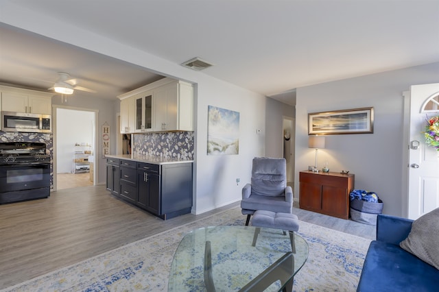 living room featuring light wood-style floors, visible vents, and a ceiling fan