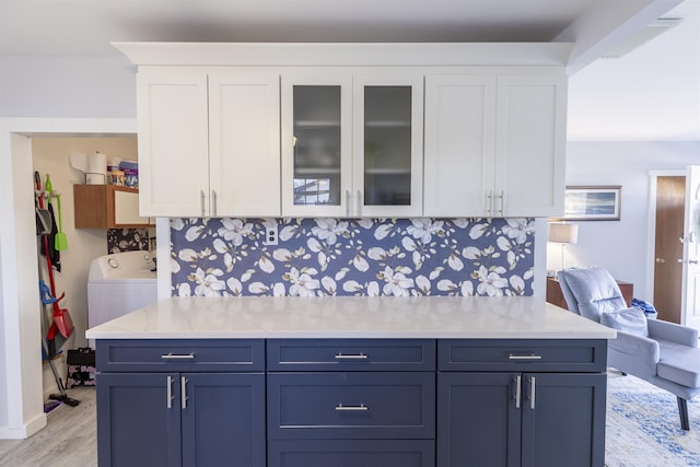 kitchen featuring light wood finished floors, tasteful backsplash, glass insert cabinets, white cabinetry, and washer / dryer