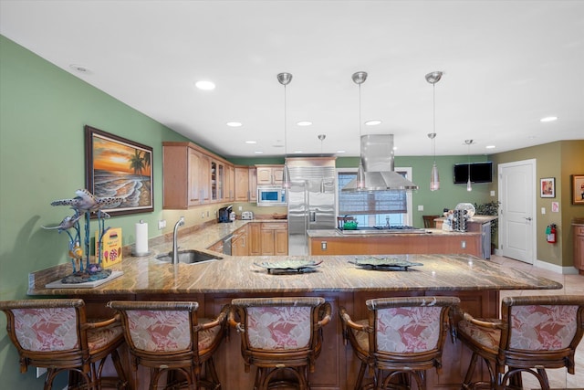 kitchen featuring kitchen peninsula, wall chimney range hood, sink, built in appliances, and hanging light fixtures