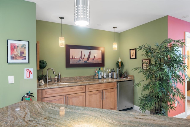 bar with light stone counters, sink, decorative light fixtures, and fridge