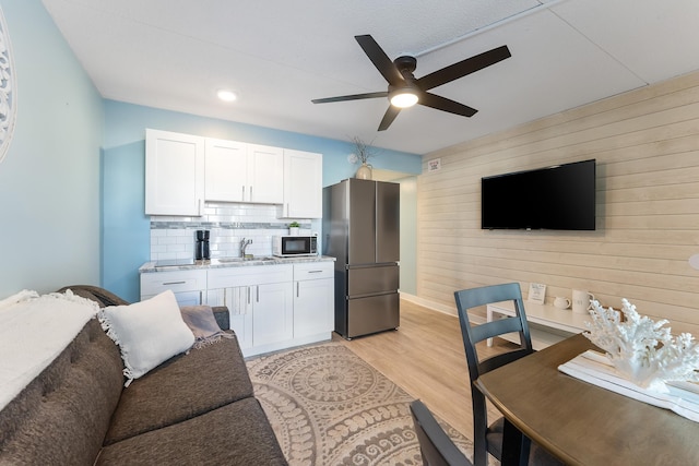 kitchen featuring a sink, white cabinets, backsplash, freestanding refrigerator, and light wood finished floors