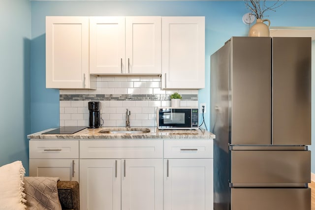 kitchen featuring tasteful backsplash, white cabinets, light stone counters, black appliances, and a sink