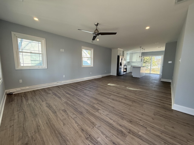 unfurnished living room with baseboards, dark wood-style flooring, a wealth of natural light, and a ceiling fan