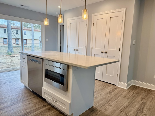 kitchen with baseboards, appliances with stainless steel finishes, decorative light fixtures, and light wood-style floors