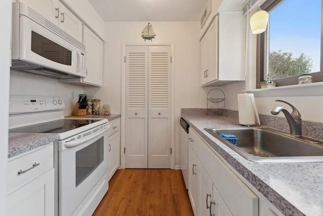 kitchen with white appliances, sink, wood-type flooring, decorative light fixtures, and white cabinetry