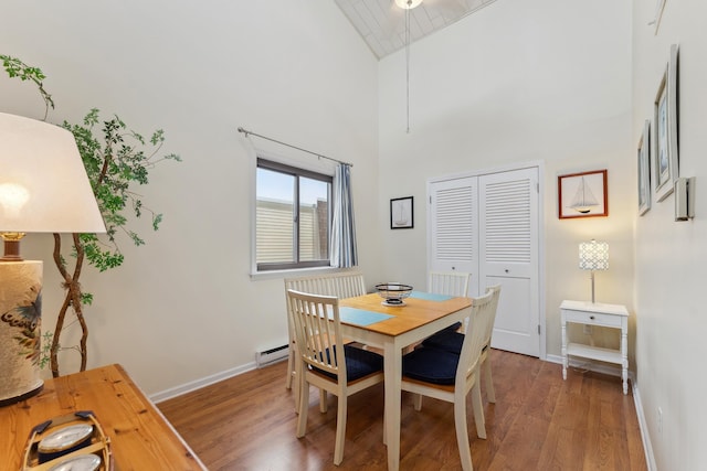 dining space with dark hardwood / wood-style flooring, high vaulted ceiling, and a baseboard heating unit