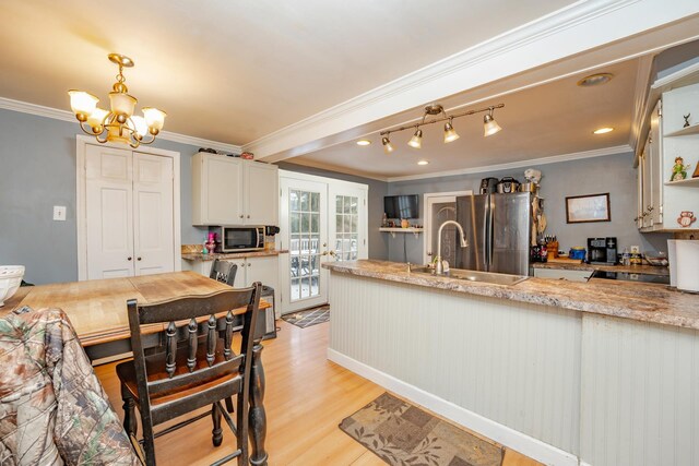 kitchen with stainless steel appliances, a sink, light wood-type flooring, light stone countertops, and decorative light fixtures