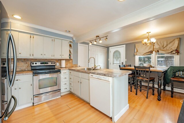 kitchen with white cabinets, appliances with stainless steel finishes, a peninsula, light countertops, and a sink