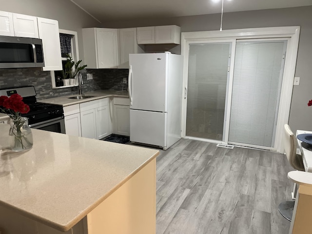 kitchen featuring gas stove, white fridge, white cabinetry, and backsplash