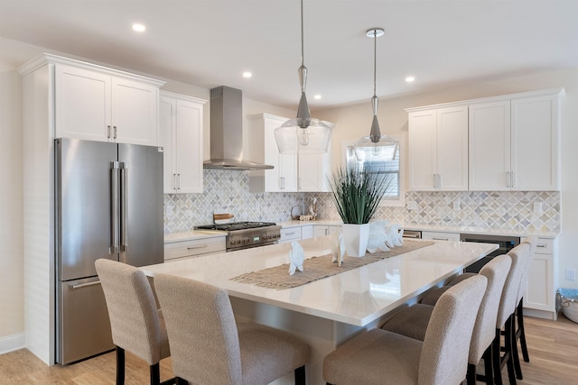 kitchen with wall chimney exhaust hood, decorative light fixtures, a center island with sink, high quality appliances, and white cabinets