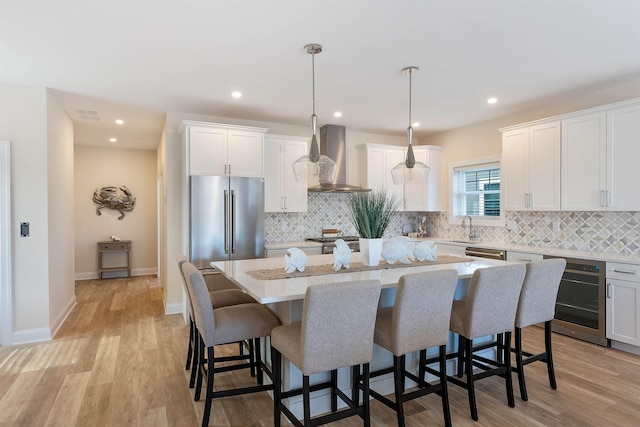 kitchen with pendant lighting, wall chimney range hood, appliances with stainless steel finishes, white cabinets, and a kitchen island