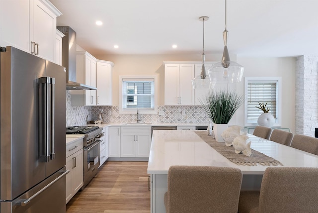 kitchen featuring decorative light fixtures, high quality appliances, sink, white cabinets, and wall chimney exhaust hood