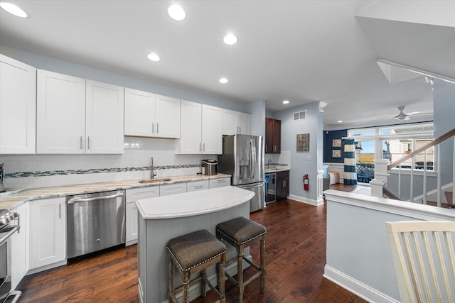 kitchen featuring white cabinetry, sink, stainless steel appliances, dark hardwood / wood-style flooring, and a breakfast bar area