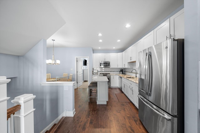 kitchen featuring white cabinets, appliances with stainless steel finishes, decorative light fixtures, a kitchen island, and a breakfast bar area