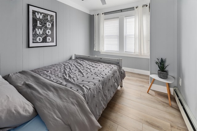 bedroom with a baseboard heating unit, light wood-type flooring, and baseboards