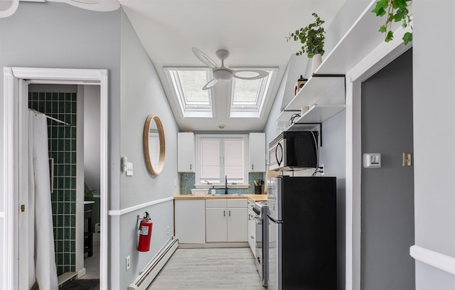 kitchen featuring a skylight, stainless steel appliances, a baseboard radiator, white cabinets, and a sink