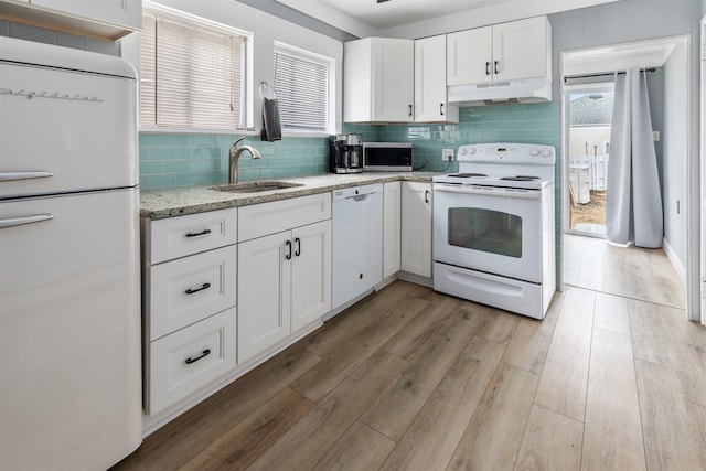 kitchen featuring light wood-style flooring, under cabinet range hood, white appliances, a sink, and decorative backsplash