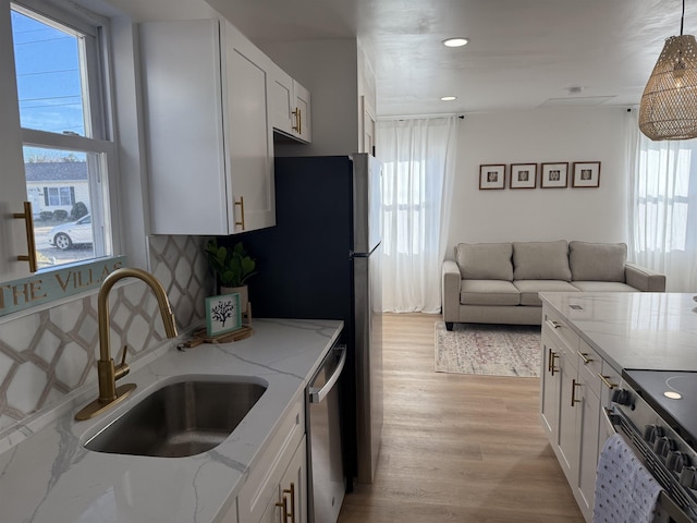 kitchen with light stone counters, stainless steel appliances, a sink, light wood finished floors, and plenty of natural light