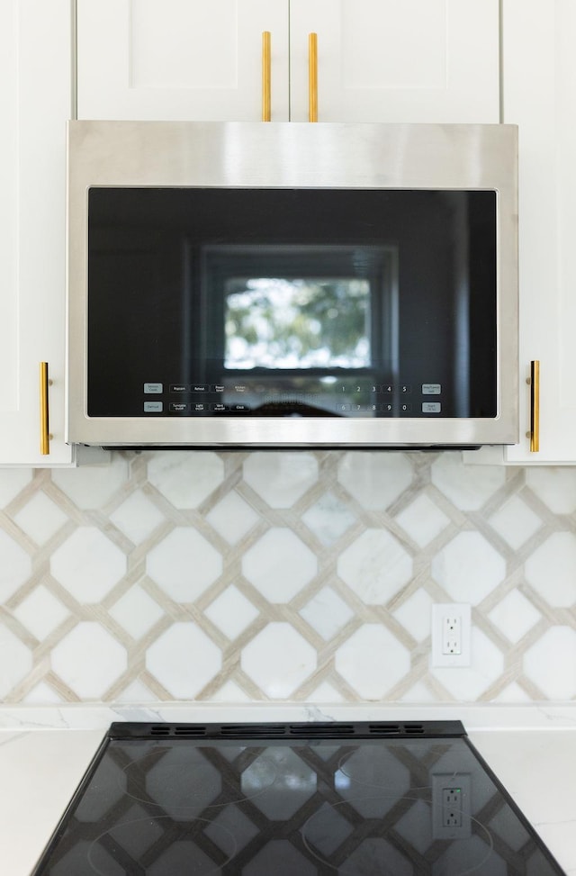 room details featuring light countertops, tasteful backsplash, stainless steel microwave, and white cabinets