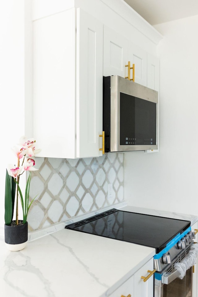 kitchen featuring light stone countertops, white cabinetry, appliances with stainless steel finishes, and decorative backsplash