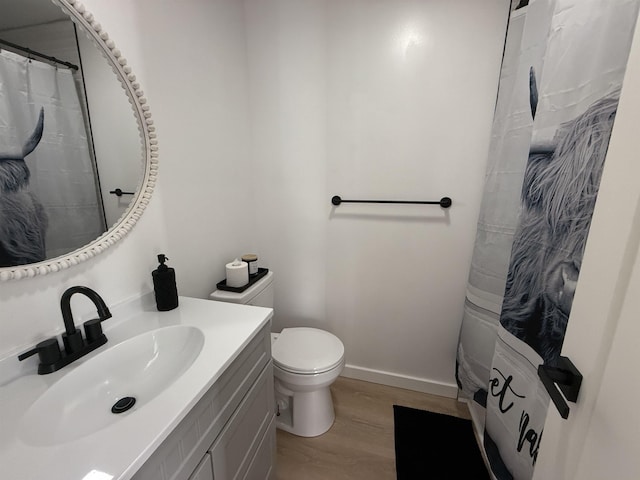 bathroom with curtained shower, toilet, vanity, wood finished floors, and baseboards