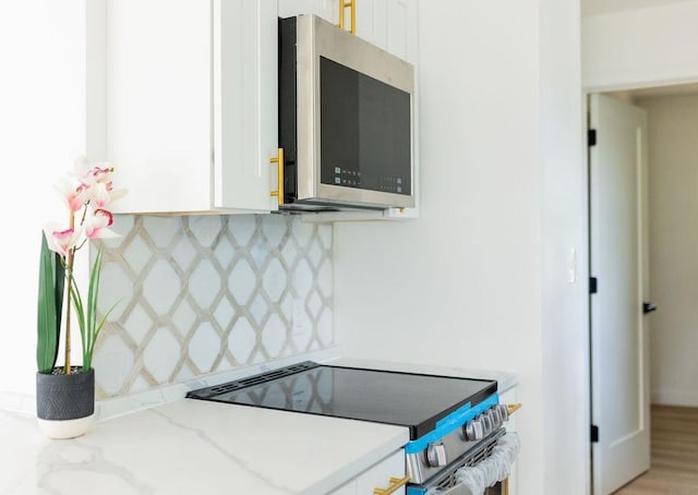 kitchen featuring stainless steel microwave, range with electric stovetop, backsplash, and white cabinetry