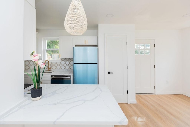 kitchen featuring dishwashing machine, light stone counters, light wood-style floors, freestanding refrigerator, and tasteful backsplash