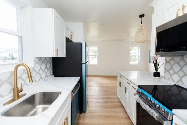 kitchen with light wood-style flooring, appliances with stainless steel finishes, decorative light fixtures, white cabinetry, and a sink