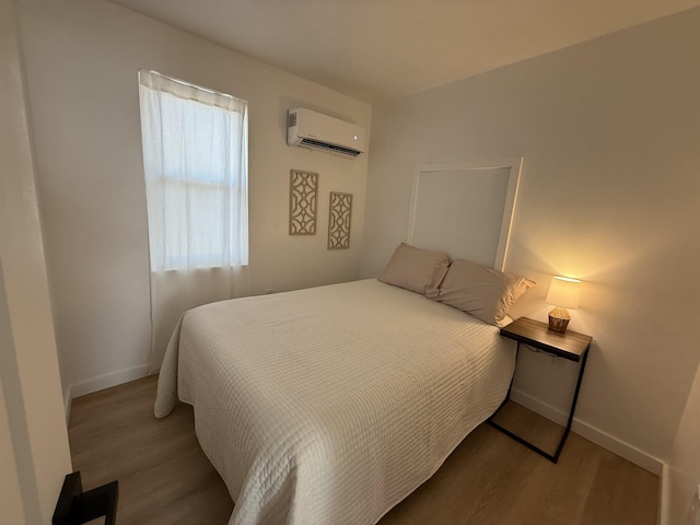 bedroom featuring a wall mounted air conditioner, wood finished floors, and baseboards