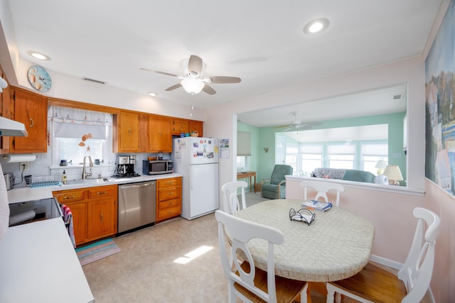 kitchen featuring stainless steel appliances, a sink, a healthy amount of sunlight, light countertops, and brown cabinetry