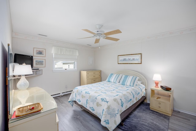 bedroom featuring a ceiling fan, visible vents, baseboard heating, and wood finished floors