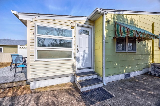 entrance to property with visible vents, central AC unit, crawl space, fence, and a deck