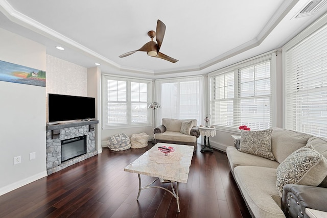 living room featuring a raised ceiling, ceiling fan, dark wood-type flooring, crown molding, and a fireplace