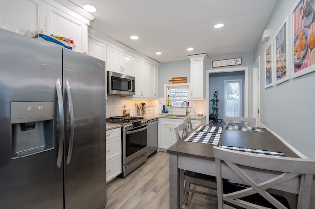 kitchen featuring stainless steel appliances, light wood-style flooring, decorative backsplash, white cabinetry, and a sink