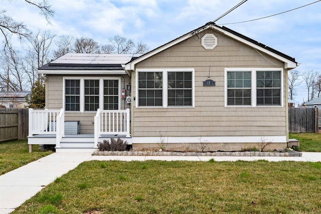 bungalow featuring a front yard, roof mounted solar panels, and fence