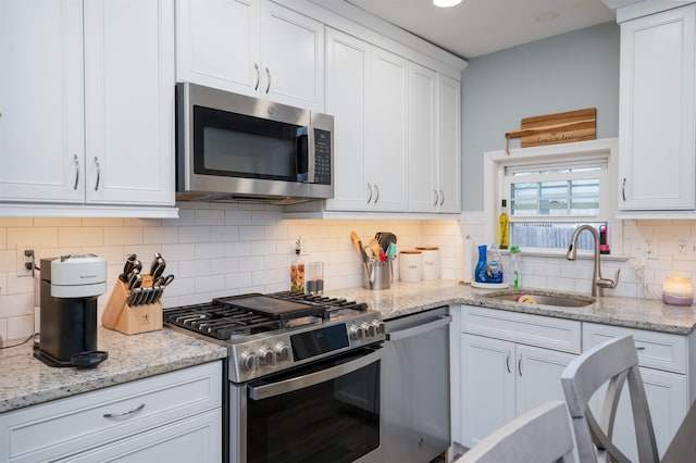 kitchen with a sink, white cabinetry, appliances with stainless steel finishes, backsplash, and light stone countertops