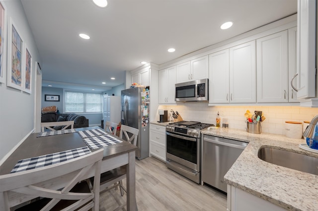 kitchen with white cabinetry, appliances with stainless steel finishes, light stone counters, and backsplash