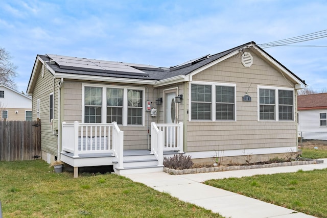 bungalow-style home with a front yard, fence, and roof mounted solar panels