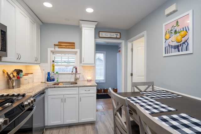 kitchen with light stone counters, a sink, white cabinets, appliances with stainless steel finishes, and tasteful backsplash