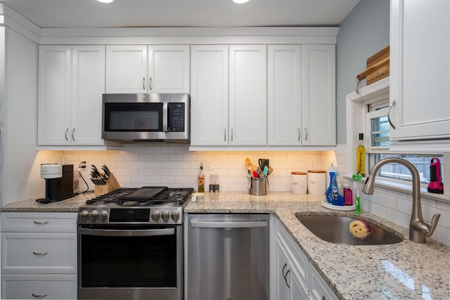 kitchen featuring light stone counters, stainless steel appliances, a sink, white cabinets, and decorative backsplash